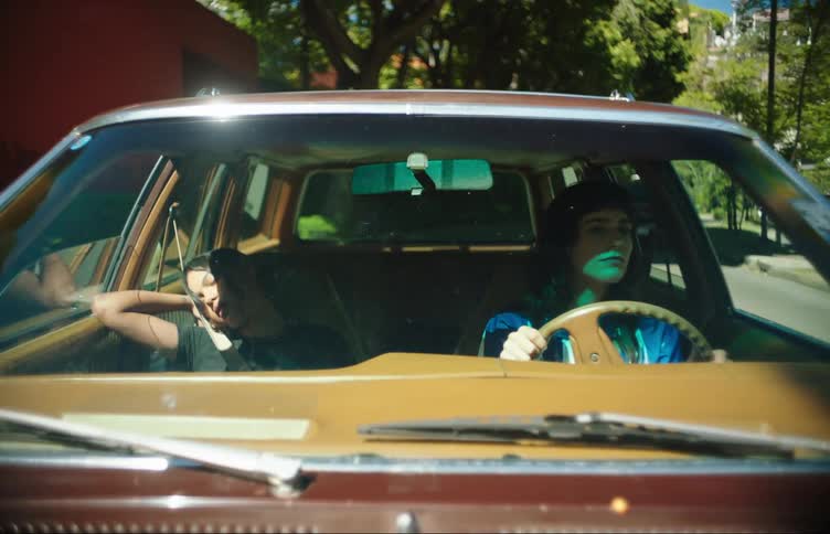 Adult woman drives through town while a younger female sleeps in passenger seat