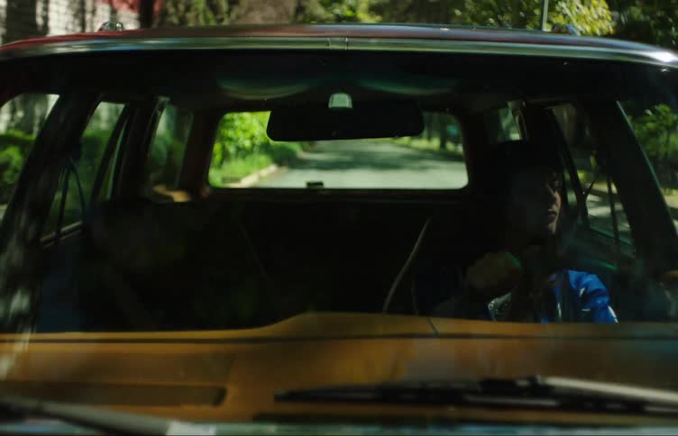View from outside on the front windshield of a vehicle with a woman driving and a young girl sleeping next to her