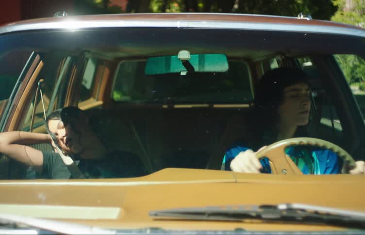 A teenage girl drives a car while her friend sleeps