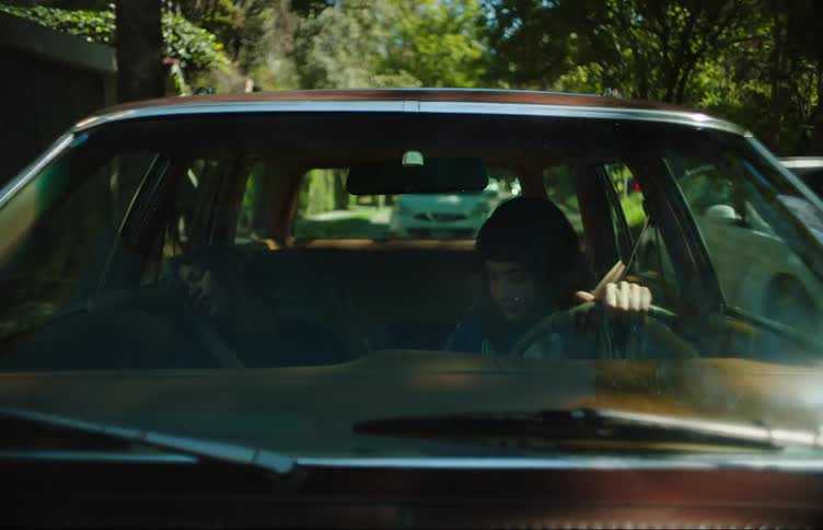 Car windshield view of two young women driving a vehicle on an urban street