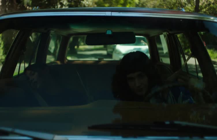 Two young women in a car talking one of them driving and the other leaning to the side and falling asleep