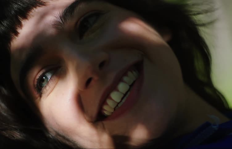 Portrait of a young woman with light eyes smiling while reflecting the shadow of tree branches and leaves on her face