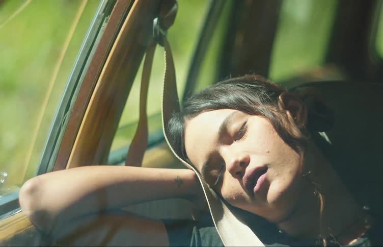 A young woman in a cars passenger seat sleeping with her arm against the window and her head resting in her hands not reacting to the cars movements