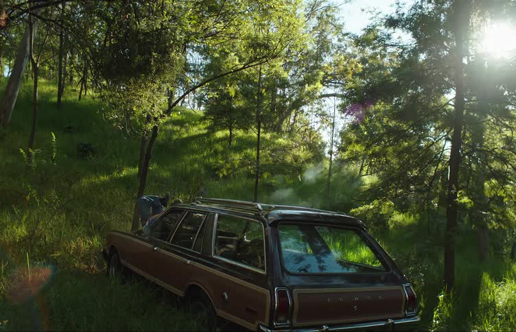Car parked on a hill in the forest with a person lying on the hood smoking