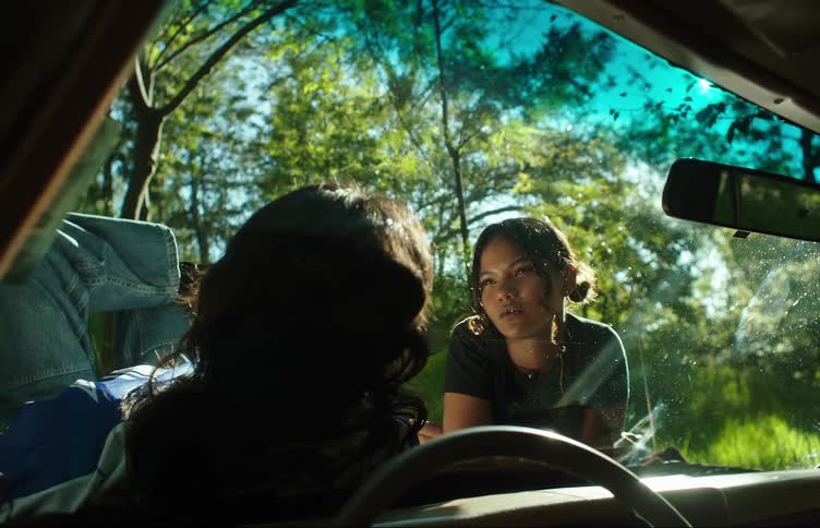 Two young women and men lying on the hood of the car talking and smoking