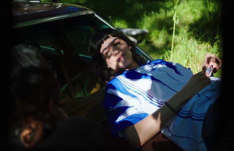 Two young women lying on the hood of a car lighting a cigarette and smoking