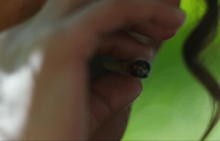 Woman smiles while smoking a hand rolled cigarette outdoors