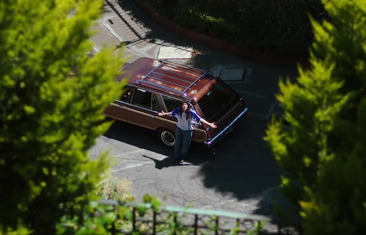 A young woman leans against a station wagon motioning yelling at her friend