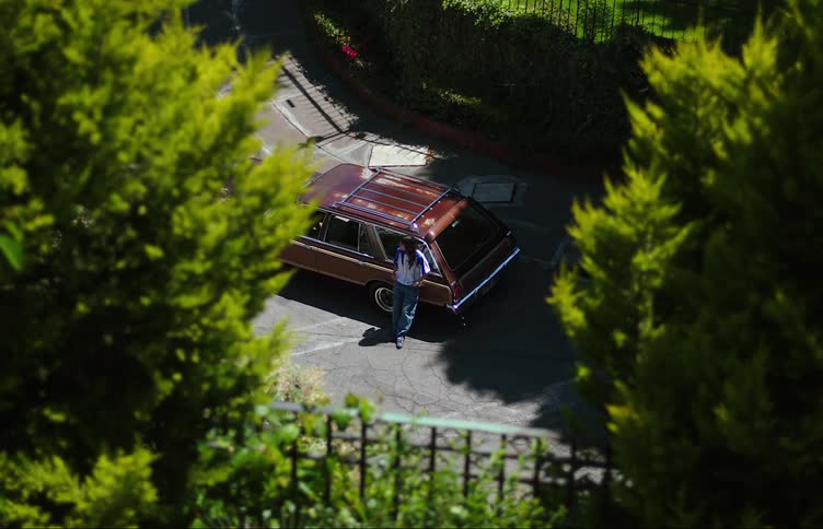 A young woman leaning against a family car impatiently calling for someone else to join her