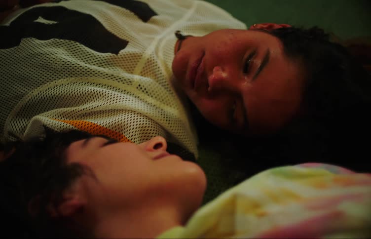 Portrait of two young women lying on the carpet looking at each other talking and smiling