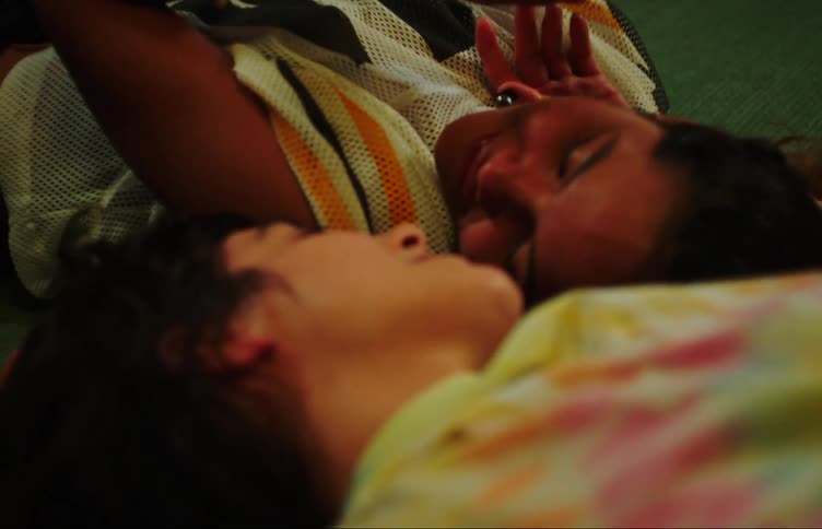 Two young women lying on the floor together their hands joined in the air then lowered and caressing each other