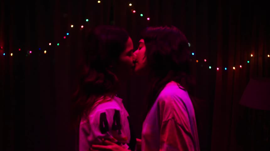 Two young women dance together indoors at night and kiss
