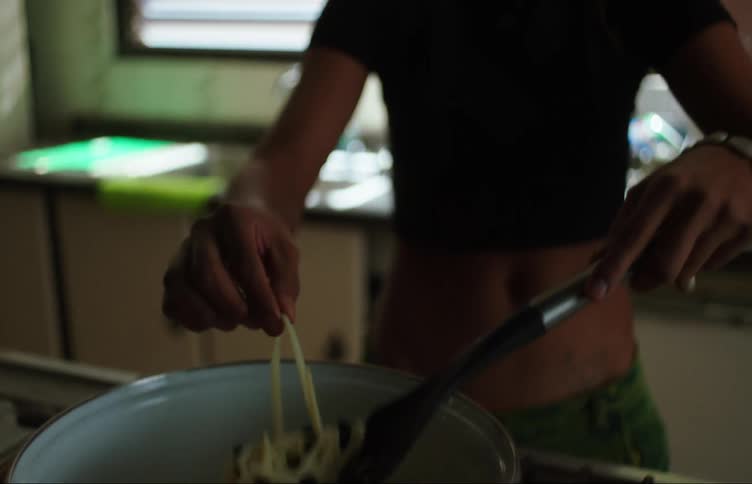 A person is sitting at the sink and then takes a pasta that is cooking on the stove and throws it at the wall