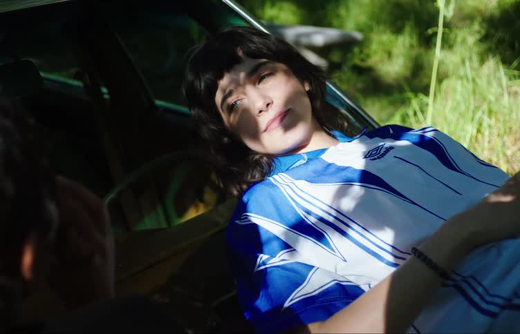 Two young woman share a smoke laying on the hood of a car