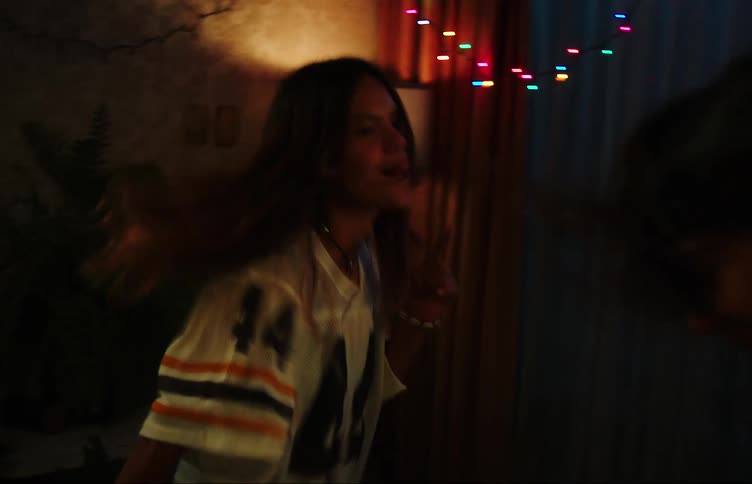 Two teenage girls dancing with hands raised in a dimly lit room with colorful lights
