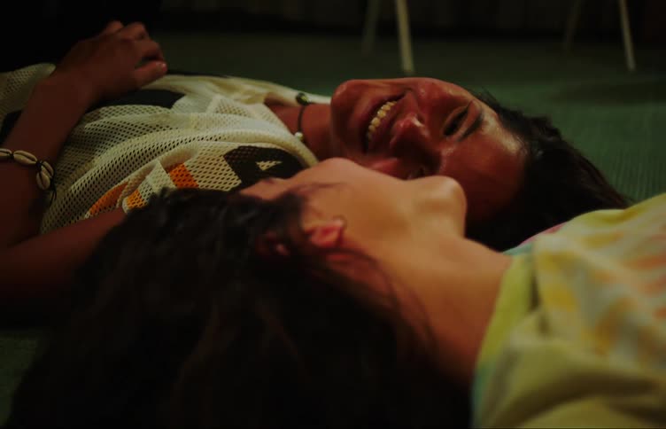 Two young girls lying on the carpet looking at each other and laughing