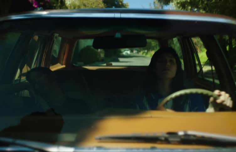 A girl drives a car through the neighborhood while her friend sleeps