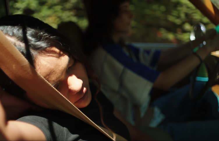A young woman drives a car another is asleep in the passenger seat