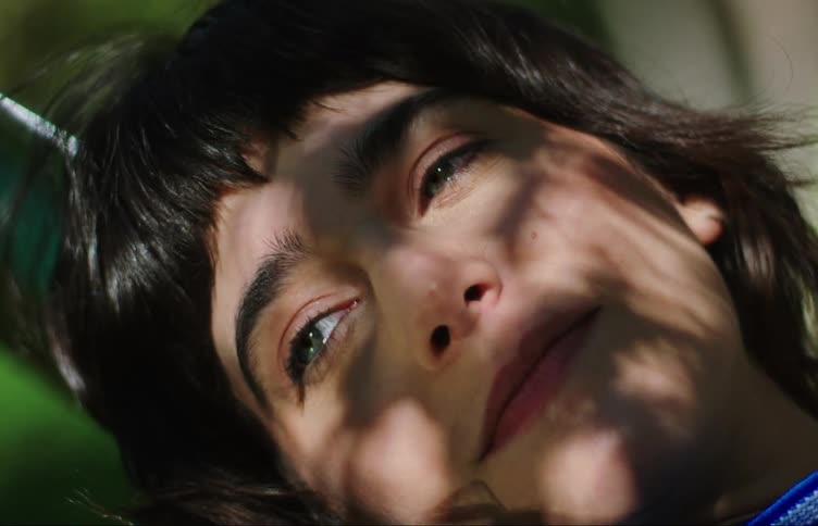 Portrait of a young woman lying down talking and with the shadow of tree leaves on her face