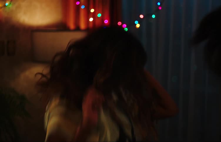 Two teenage girls dancing in a dimly lit room with colorful lights