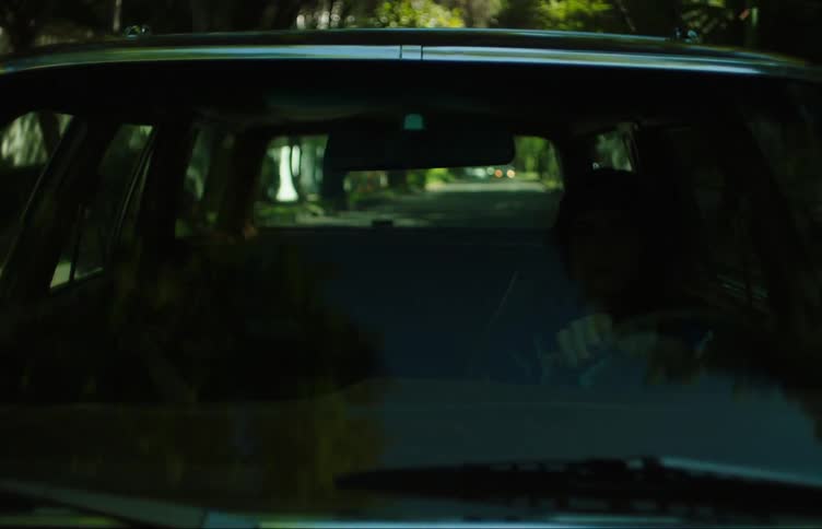 Teenage girl driving a car around the neighborhood while a friend sleeps