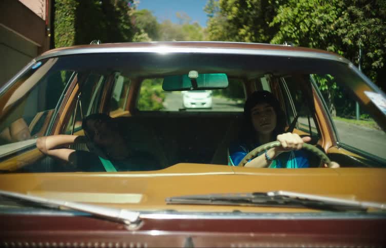 A girl drives a car through the neighborhood while her friend sleeps