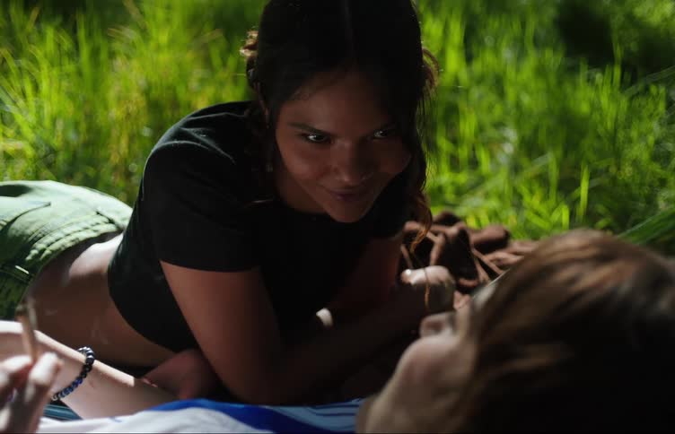 Friends lying on the hood of a car in a field talking and smoking a cigarette