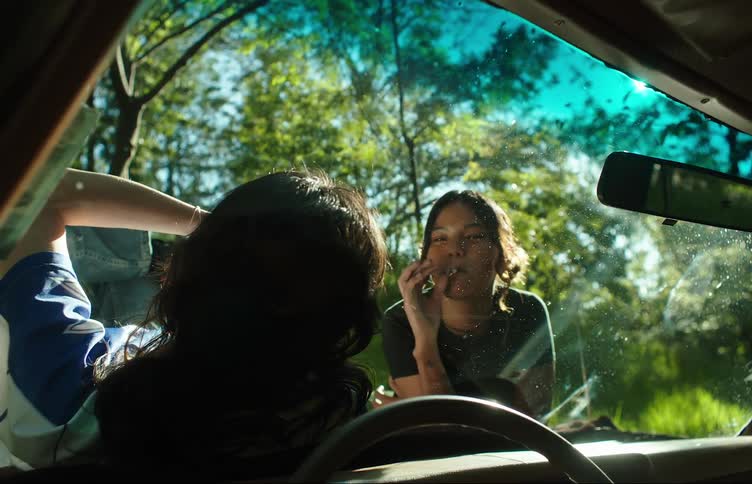 A couple of girls smoking over the hood of a car