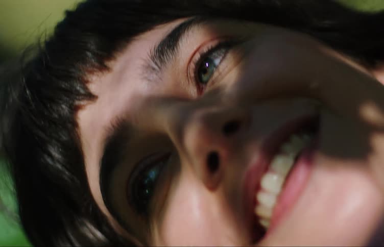 Face of a young woman lying outdoors smiling with the reflection of tree leaves on her face
