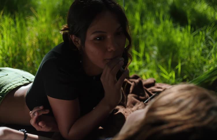 Two young women lying on the hood of a car while talking and smoking a cigarette