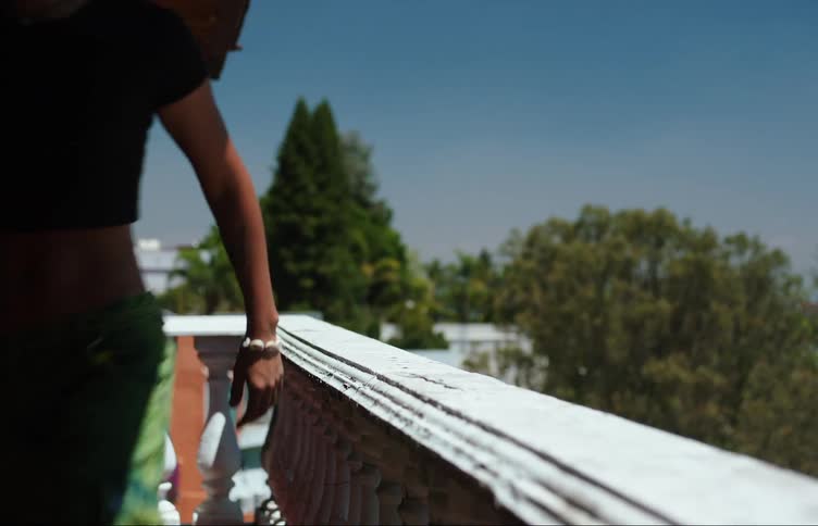 A young woman walks out and leans on a balcony railing talking to someone