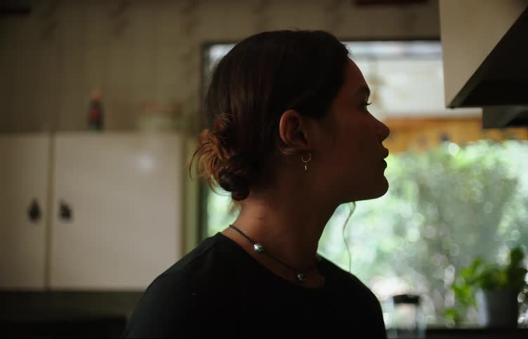 A young woman in the kitchen is distracted by something outside and angrily leaves to check