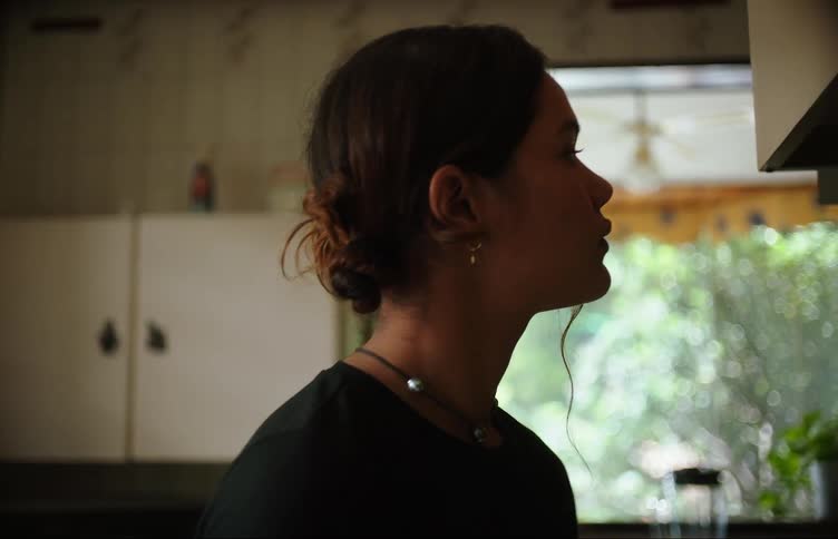 A young woman is in a kitchen annoyed when something in another room calls her attention and she rushes to see what it is