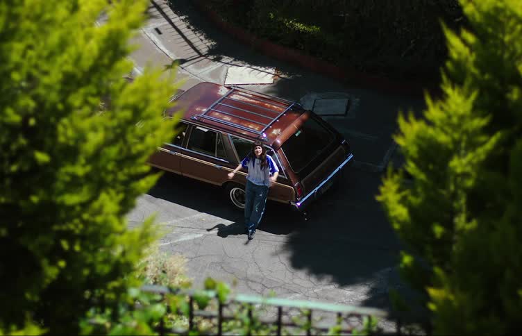 A young woman leans against a station wagon yelling to her friend