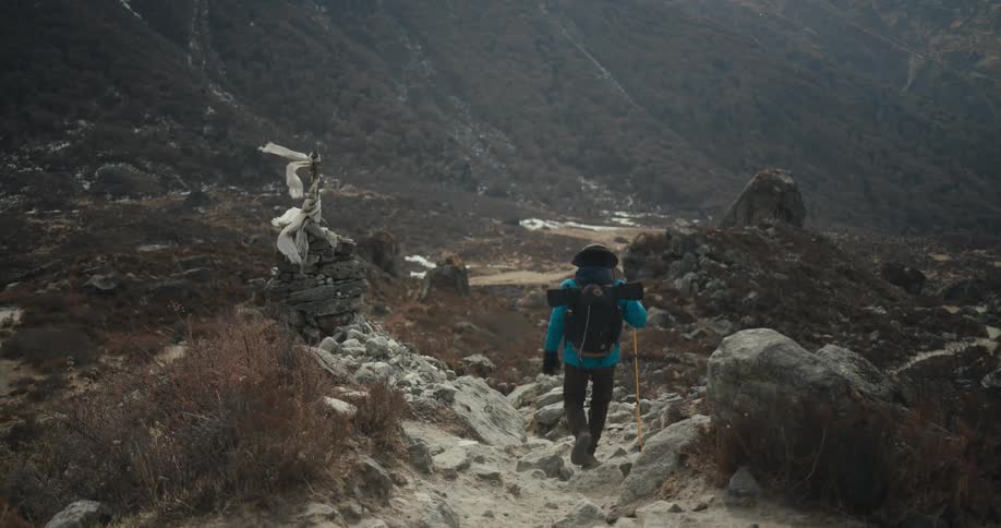 A hiker carrying a backpack walks down a rocky trail in a remote area