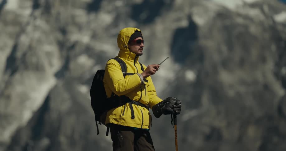 Man with hiking gear communicating on a radio while standing in outdoor environment with mountain ranges around him