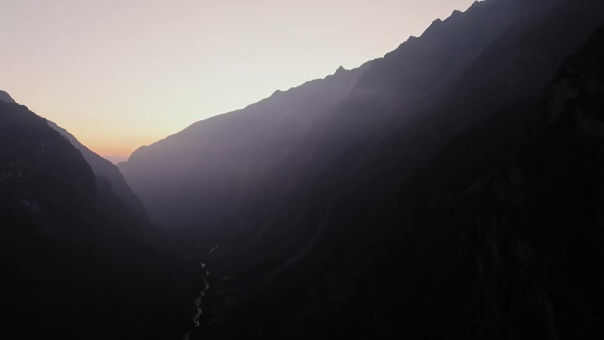 Aerial landscape of rocky mountain range with a river stream and the reddish sky on the morning horizon