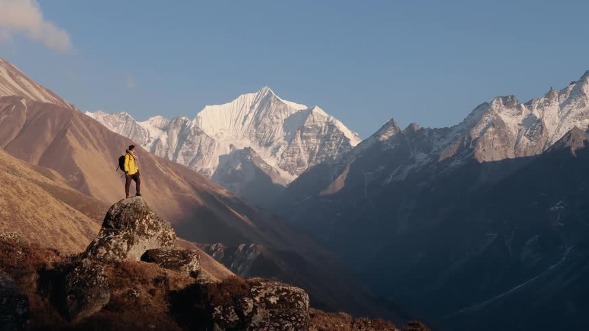 A hiker stands on a mountain ridge gazing at snowcapped peaks in the distance