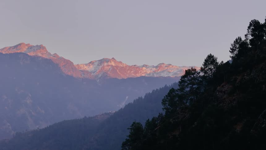 Aerial scenery of mountains with forests and on the horizon other mountains with snow on a morning