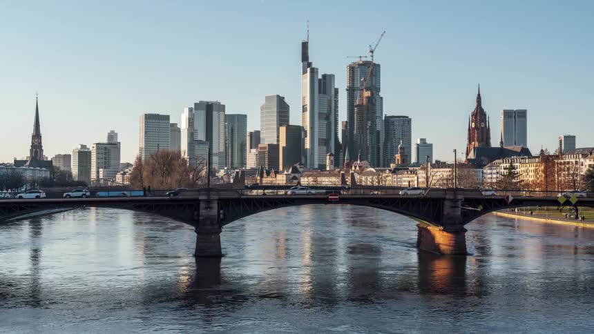 Scenery of a bridge over a flowing river overlooking a metropolis with modern buildings and skyscrapers in a day passing by in timelapse