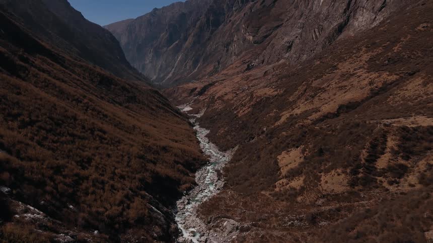 Aerial panorama of a flowing river amidst rocky mountains on a cloudless blue sky day