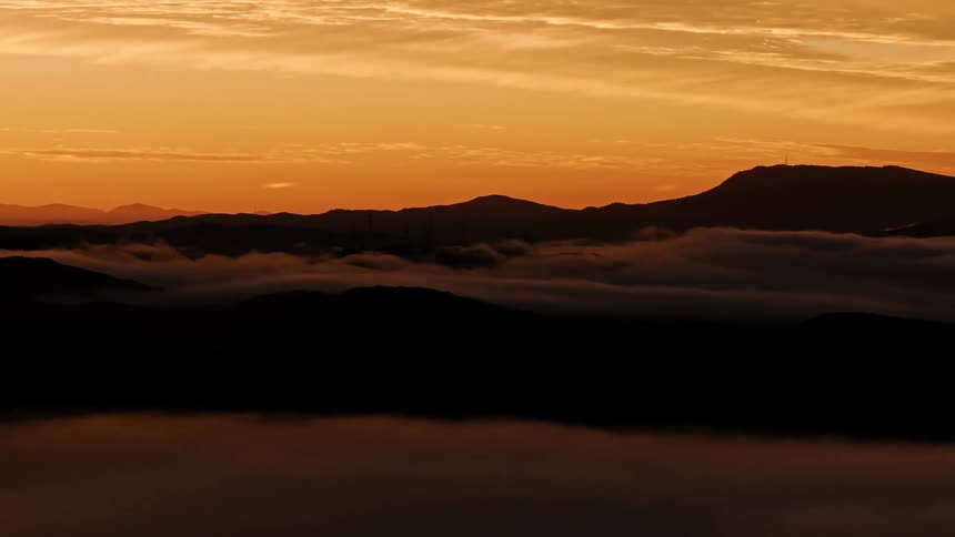 Aerial silhouette landscape of mountains with fog and an orange morning sky