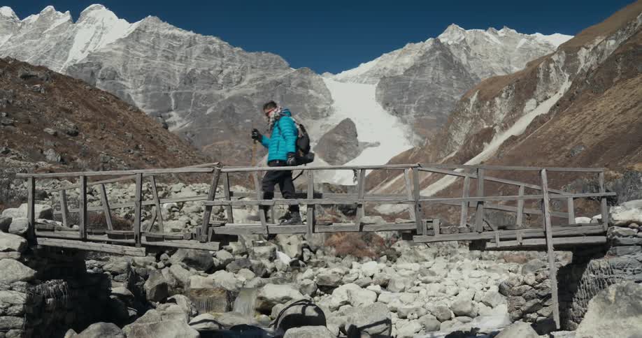 A hiker crosses a small wooden bridge next to the mountains