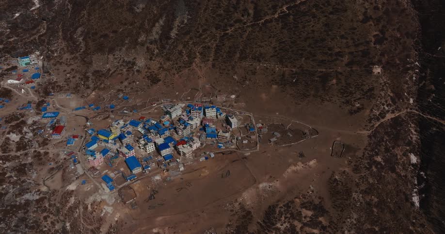 A village with several houses at the base of a mountain and the roofs of the houses are blue