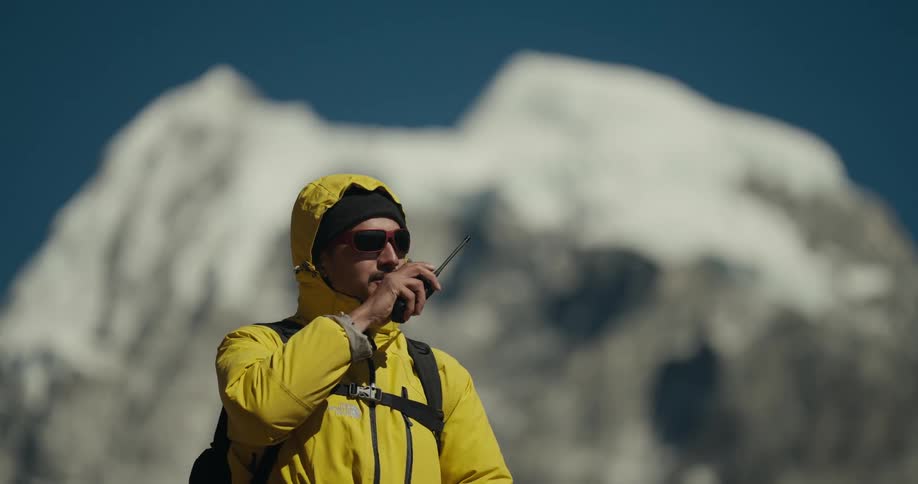 A hiker at the top of a mountain talks on a walkie talkie