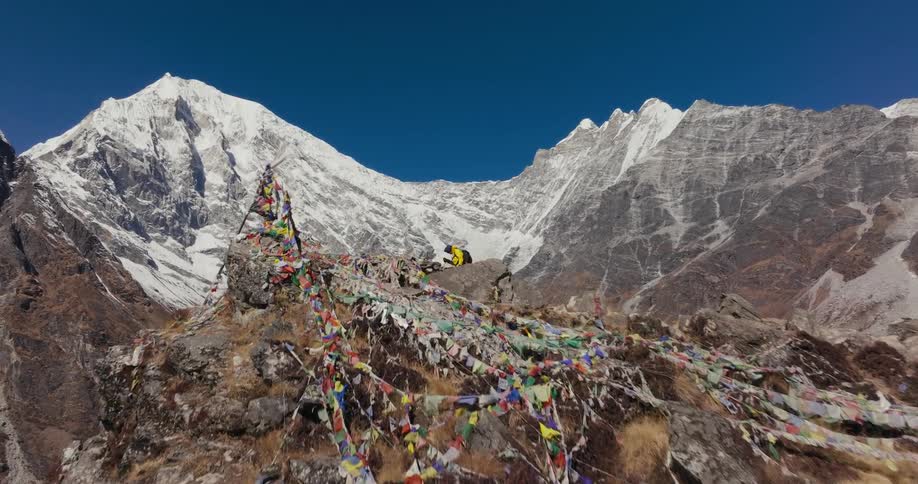 Man walking on a cliff with flags and surrounded by snowy mountain ranges in winter