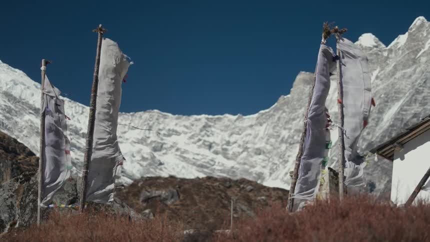 Flags on a hill of a temple with mountains around with snow