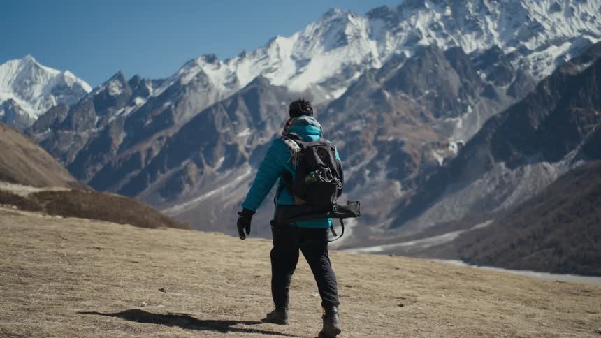 Man with equipment hiking on a hill surrounded by a natural landscape with snowy mountains