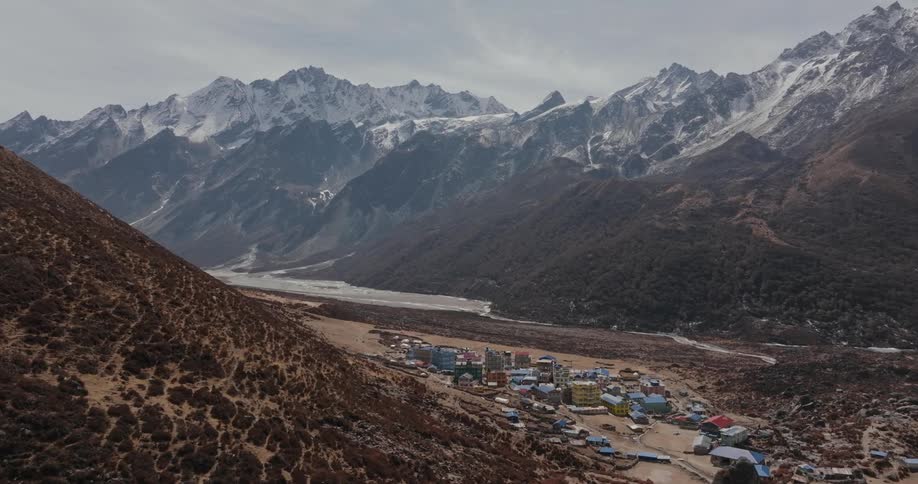 Aerial scenery of a village built on the plateau with mountain ranges and snowy reliefs around it