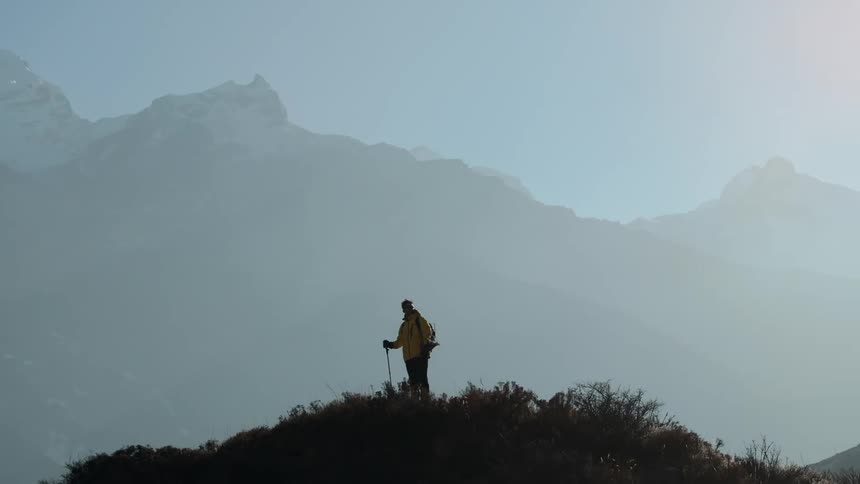 A hiker stands on a mountain ridge gazing at snowcapped peaks in the distance
